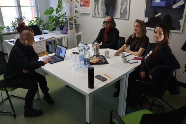 zdjęcie przedstawiające siedzących przy stole: mężczyznę i trzy kobiety. jedna z kobiet robi coś w laptopie